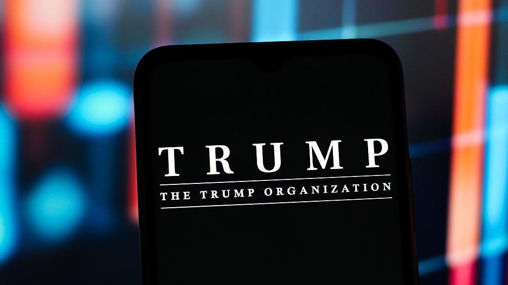 El logotipo de la Organizaci&oacute;n Trump en la pantalla de un tel&eacute;fono. 