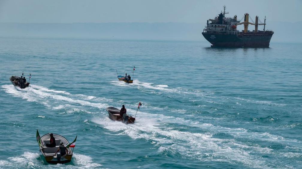 Cuatro lanchas r&aacute;pidas con banderas iran&iacute;es navegando por el Golfo P&eacute;rsico, cerca de un buque de carga general.