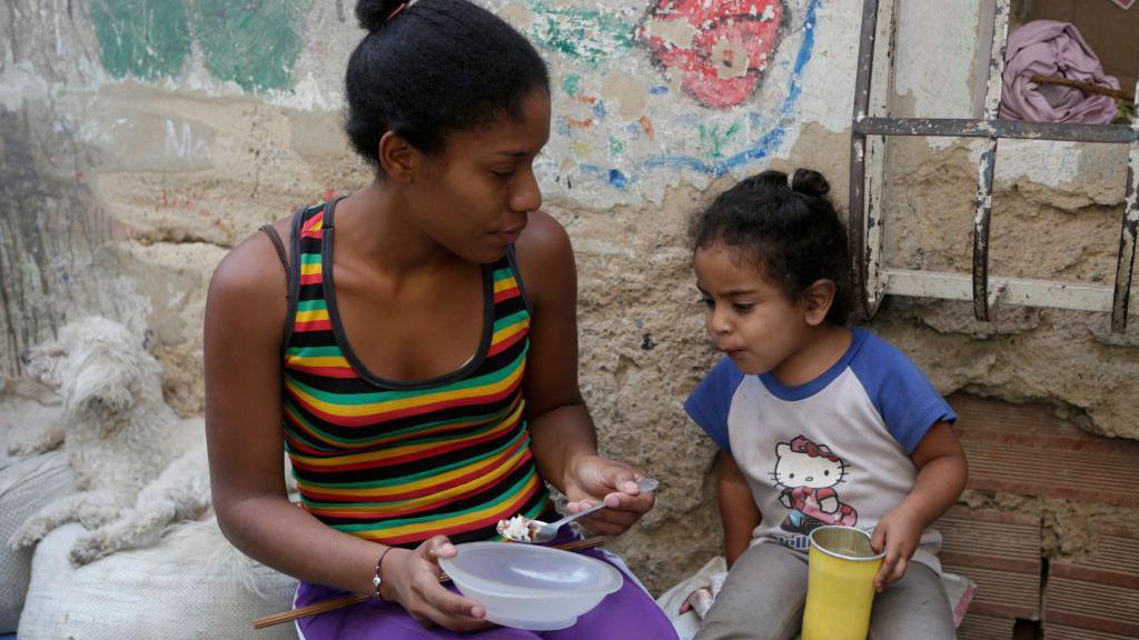 Una mujer alimenta a una ni&ntilde;a en el barrio La Bombilla en Caracas.
