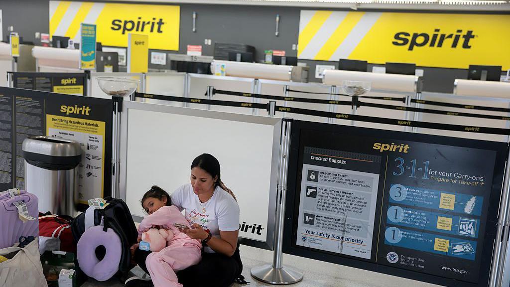 Una mujer colombiana con su hija de brazos, sentada en el counter vac&iacute;o de Spirit Airlines