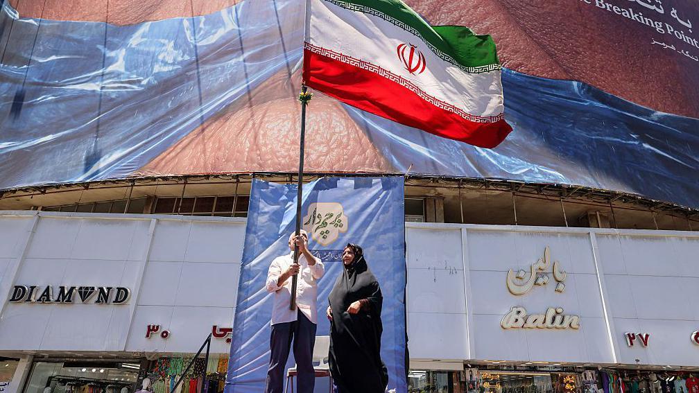 La gente alza una bandera iran&iacute; en Teher&aacute;n.