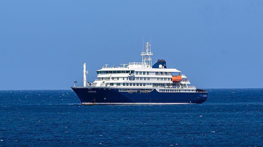 El crucero MV Hondius anclado frente al puerto de Praia, la capital de Cabo Verde, el 3 de mayo de 2026. Es una embarcaci&oacute;n de gran tama&ntilde;o, de color azul y blanco. 