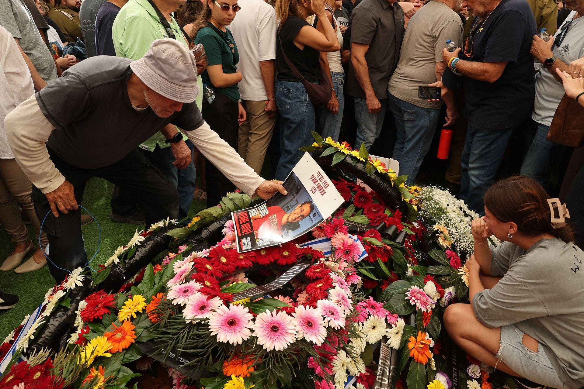 Una persona sostiene la foto de Tamir Nimrodi, un soldado israel&iacute; que muri&oacute; en cautiverio en Gaza tras ser capturado en octubre de 2023, que yace sobre un mont&oacute;n de flores rodeado de dolientes en la ciudad central israel&iacute; de Kfar Saba.16 de octubre de 2025.