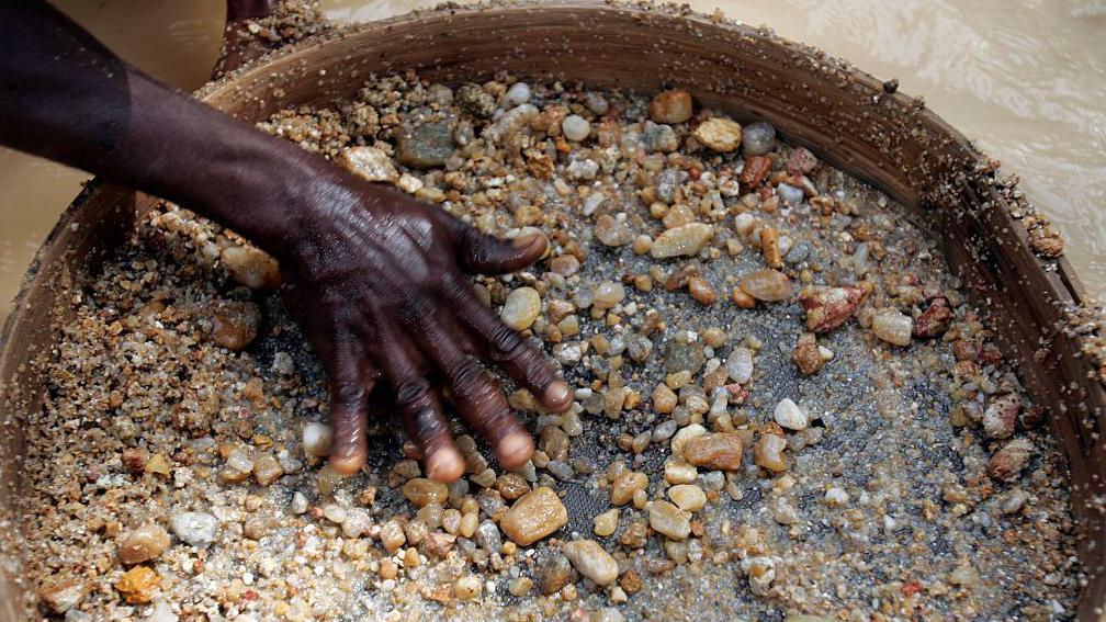 La mano de un minero de diamantes en Sierra Leona tamiza piedras m&aacute;s peque&ntilde;as con la esperanza de encontrar las preciosas gemas