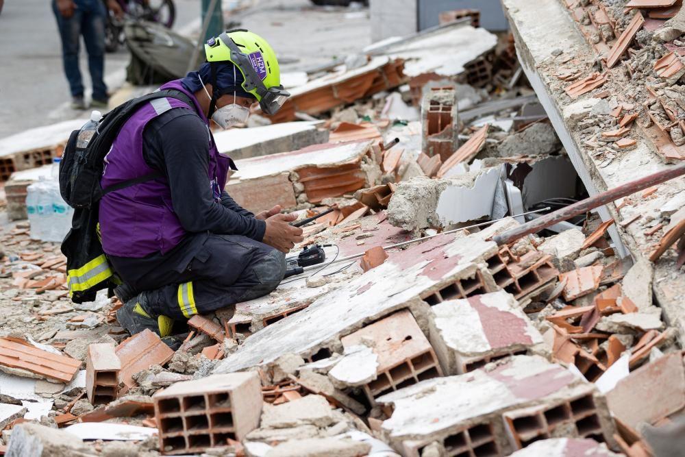 Un rescatista con casco, tapabocas y chaleco morado usa un dispositivo de detecci&oacute;n de sonido sobre los escombros de un edificio en Catia La Mar, Venezuela.