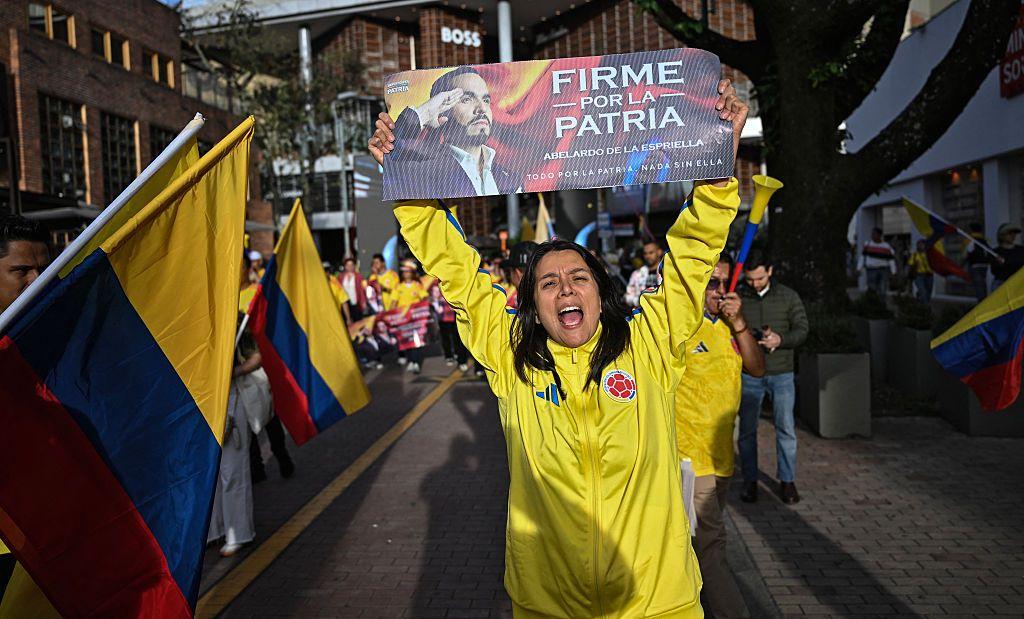 Una mujer vestida con ropa de la selecci&oacute;n de f&uacute;tbol colombiana sostiene un cartel de la campa&ntilde;a de Abelardo de la Espriella con su imagen y el esl&oacute;gan "Firme por la patria" en Bogot&aacute; el 12 de junio de 2026.