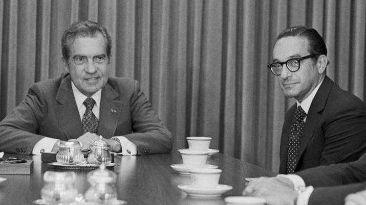 Una fotograf&iacute;a en blanco y negro de Richard Nixon y Alan Greenspan. Est&aacute;n sentados ante una mesa cubierta de tazas de t&eacute;.
