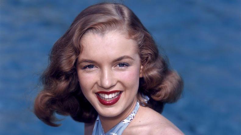 Marilyn Monroe sonr&iacute;e en una imagen de 1946, tiene elcabello casta&ntilde;o y los labios pintados.