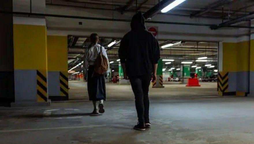 Un hombre con la capucha subida sigue a una mujer por un aparcamiento subterr&aacute;neo tenuemente iluminado.