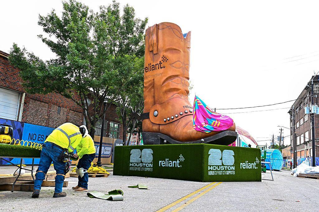 Una calle en Houston, Texas en la que se est&aacute; instalando una zona para que fan&aacute;ticos del f&uacute;tbol puedan disfrutar los partidos. Hay ds trabajadores instalando unas mesas y detr&aacute;s de ellos se ve una inmensa bota texana de adorno que est&aacute; instalada en la mitad de la calle