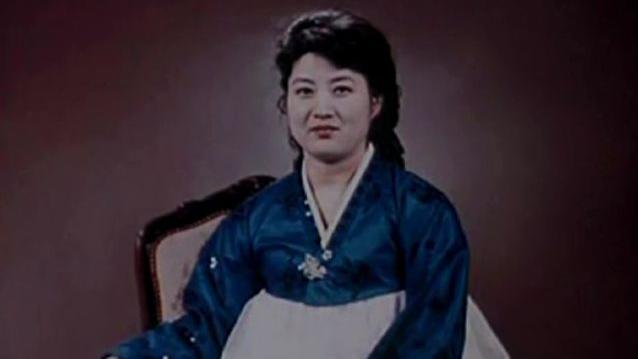 Ko Yong-hui, que debe de tener entre treinta y cuarenta a&ntilde;os, lleva un vestido tradicional coreano azul y blanco y sonr&iacute;e a la c&aacute;mara