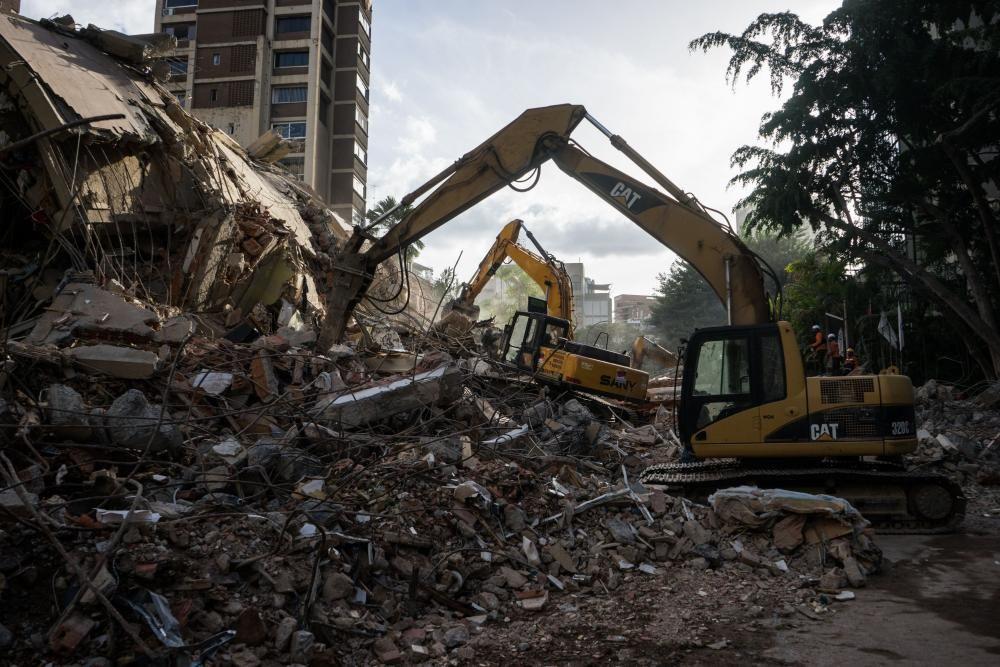 Bulld&oacute;ceres amarillos trabajando junto a los escombros de un edificio en Caracas.