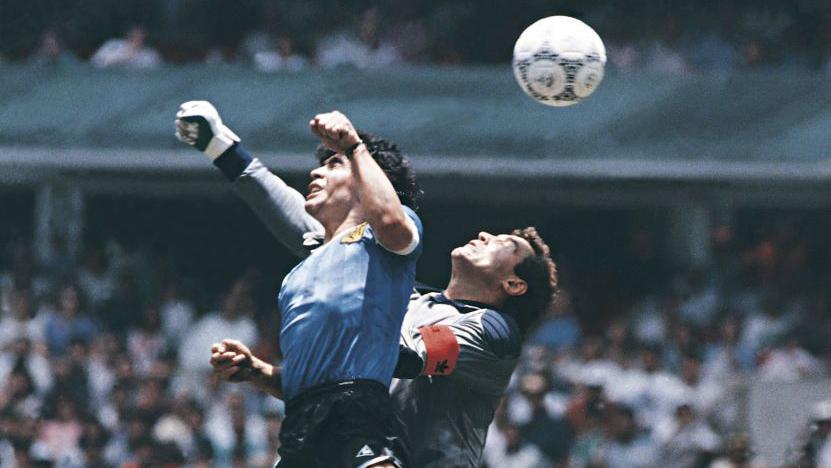 Imagen de primer plano de Diego Maradona con el pu&ntilde;o en alto golpeando la pelota en la red con Peter Shilton muy cerca. 