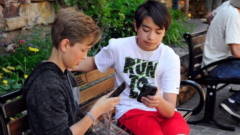 Dos ni&ntilde;os sentados mirando sus tel&eacute;fonos