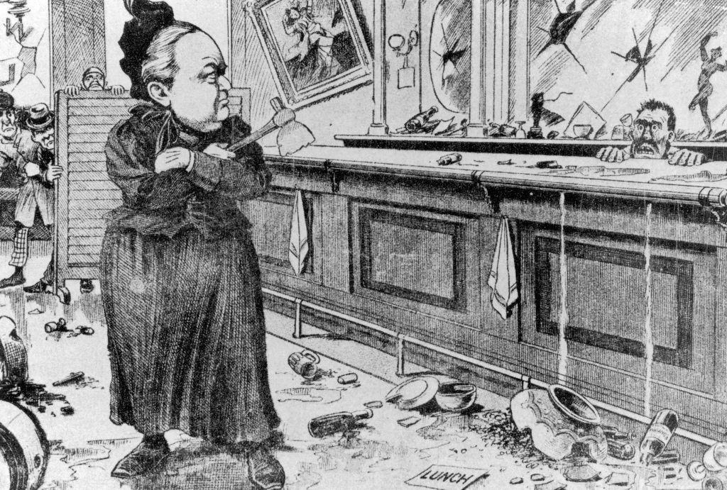Una caricatura antigua en la que se representa a Carrie Nation, con un hacha en la mano, en una cantina destrozada. el bartender la mira desde detr&aacute;s de la barra con terror. 