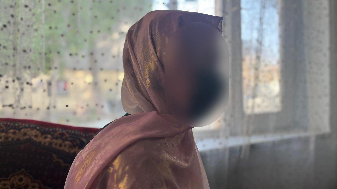 Una mujer, cubierta con velo isl&aacute;mico y la cara difuminada para ocultar su identidad, junto a una ventana. 