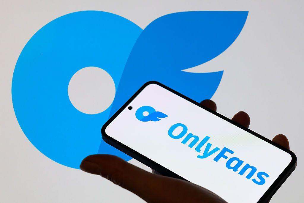 Una persona sostiene un m&oacute;vil en la mano, el cual tiene el logo de OnlyFans en azul