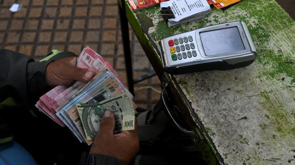 Un vendedor de loter&iacute;a sostiene un fajo de billetes de distintos colores.