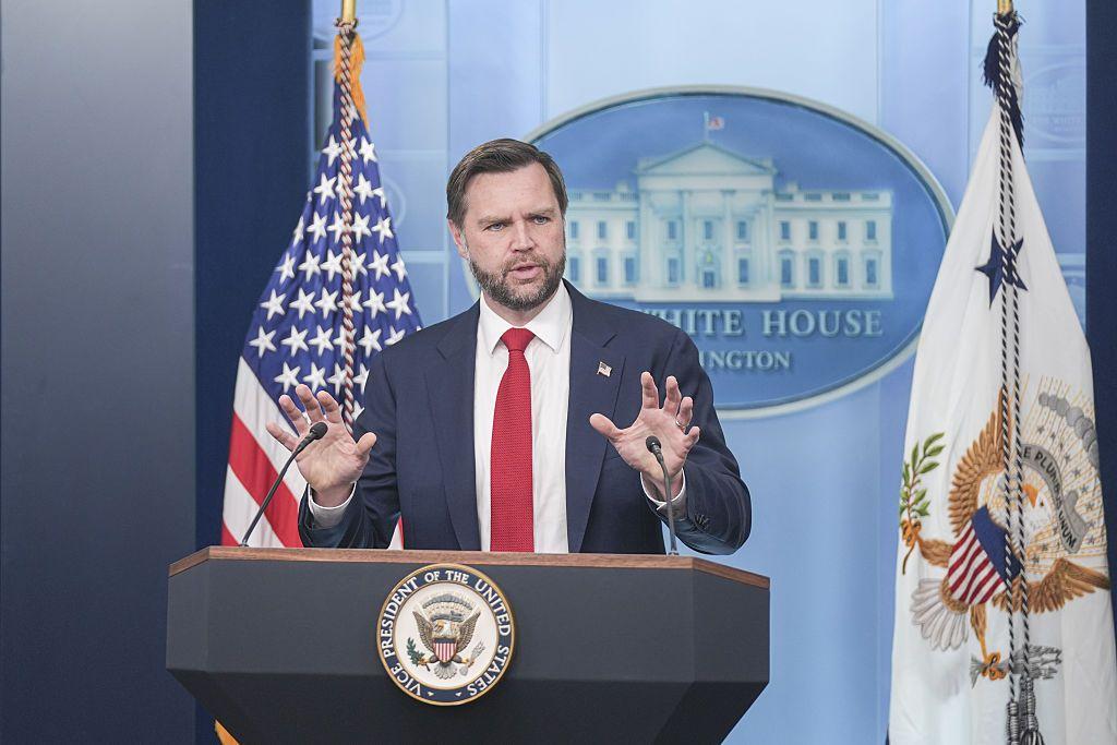 El vicepresidente de EE.UU., JD Vance, habla desde un atril durante una rueda de prensa en la Casa Blanca. Viste traje oscuro, camisa blanca y corbata roja.