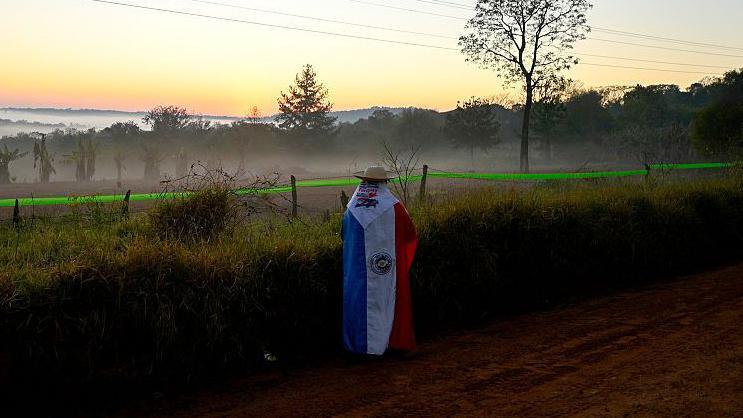 Una persona envuelta en la bandera paraguaya observa el amanecer cerca de Encarnaci&oacute;n, Paraguay.