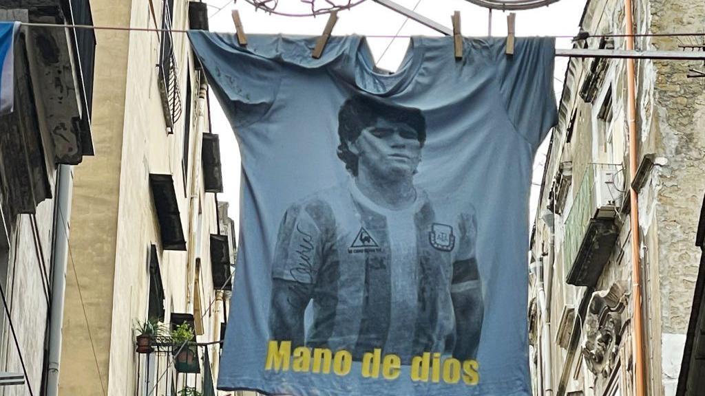 Una camiseta con el rostro de Maradona y la inscripci&oacute;n "Mano de dios" en las calles del centro hist&oacute;rico al d&iacute;a siguiente del primer aniversario de la muerte de Diego Armando Maradona el 26 de noviembre de 2021 en N&aacute;poles (Italia). 