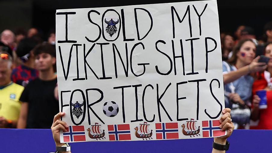 Un aficionado noruego sostiene un cartel que dice que vendi&oacute; su barco vikingo para comprar entradas para el partido durante la Copa Mundial de la FIFA 2026.