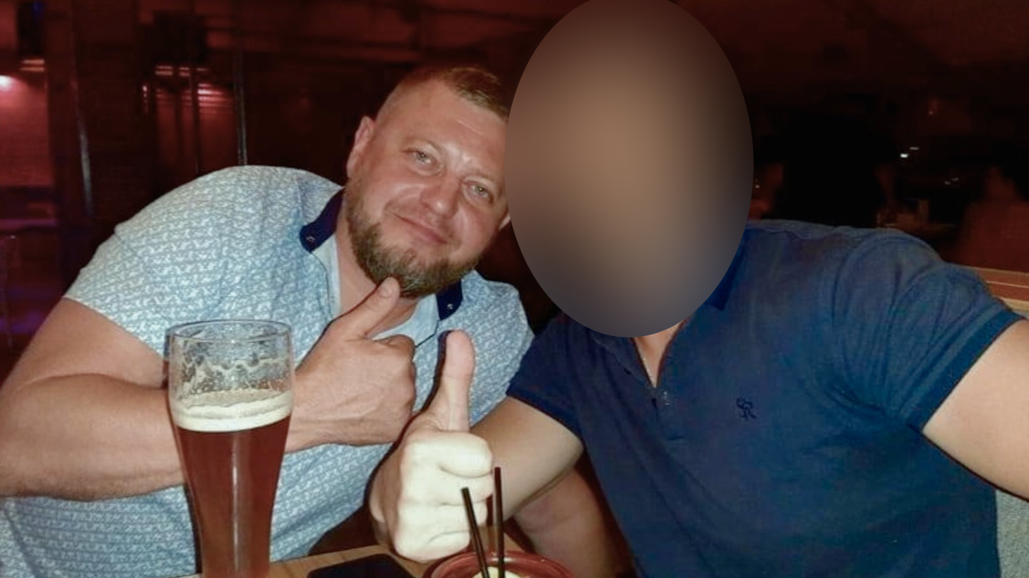 Dos hombres, con vasos grandes frente a ellos, hacen el gesto de pulgar hacia arriba a la c&aacute;mara. El de la izquierda, Ruslan Yeriomichev, lleva barba recortada y el pelo muy corto, y viste una camiseta clara con estampado. El rostro del hombre de la derecha ha sido difuminado.