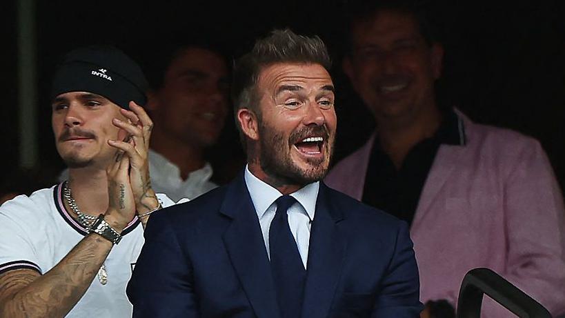 El exfutbolista ingl&eacute;s David Beckham sonr&iacute;e durante el partido de cuartos de final del Mundial de F&uacute;tbol de 2026 entre Noruega e Inglaterra en el Miami Stadium de Miami Gardens el 11 de julio. Viste un traje azul, camisa blanca y corbata azul.
