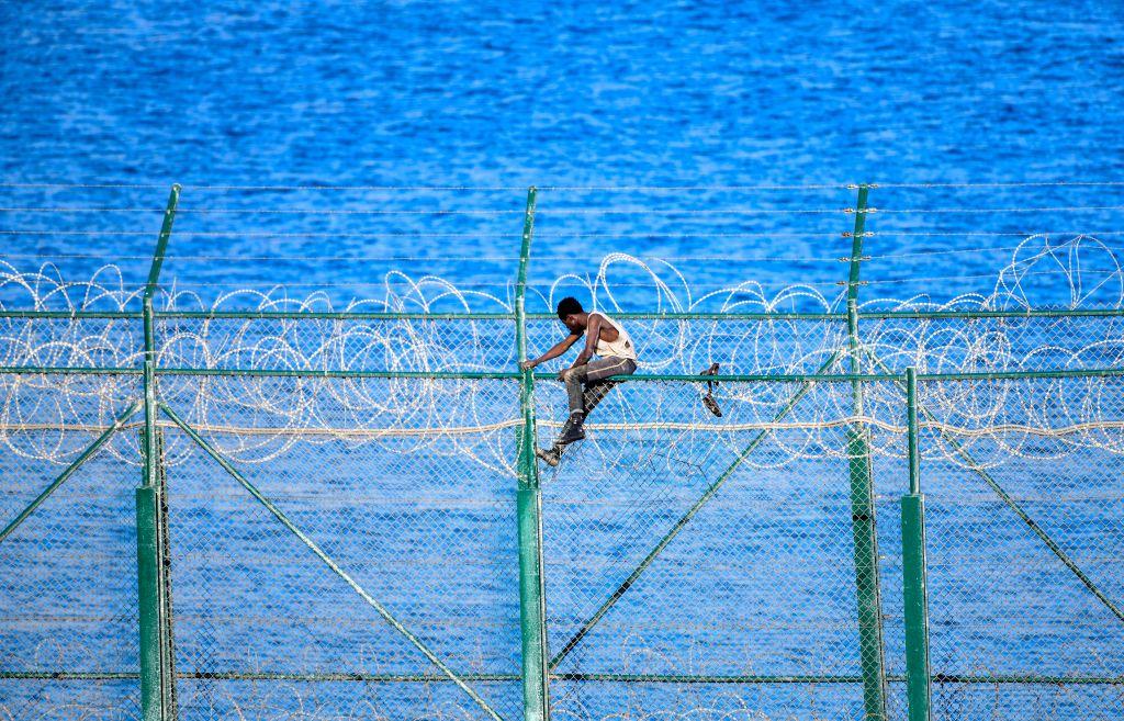 Un migrante cruza al territorio español de Ceuta trepando una valla con alambre de púas el 30 de agosto de 2019.