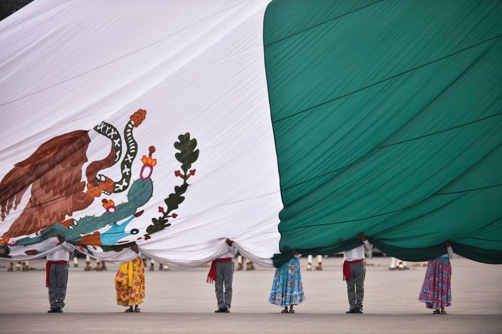 Bandera de M&eacute;xico sobre seis personas en una plaza