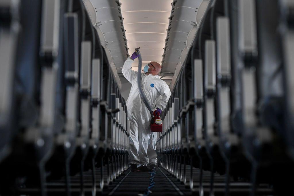 Una persona con un traje antibacterial desinfecta la cabina de un avión.