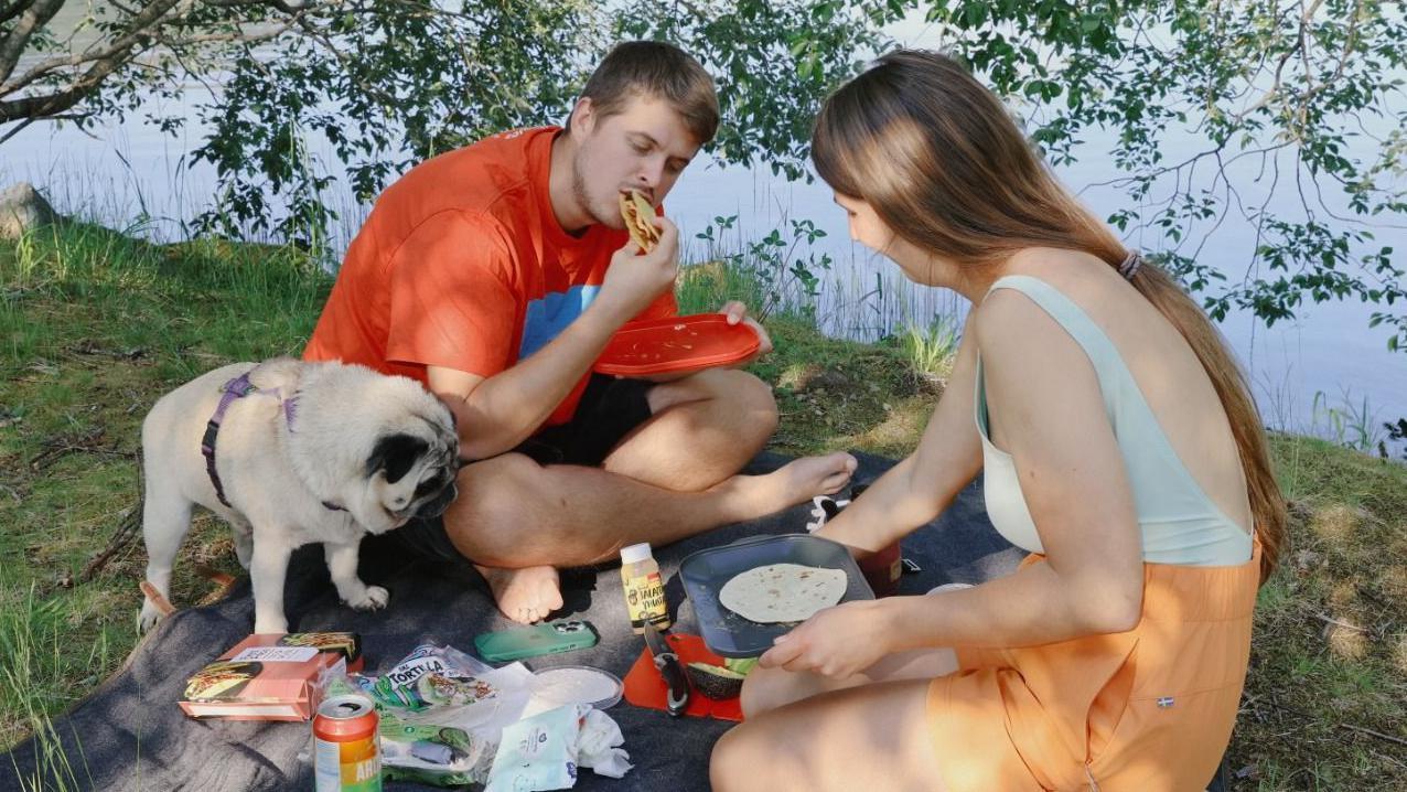 Una mujer y un hombre noruegos est&aacute;n sentados charlando de sobremesa en un comedor donde est&aacute; servido un banquete de tacos. Beben cerveza y tienen velas encendidas.