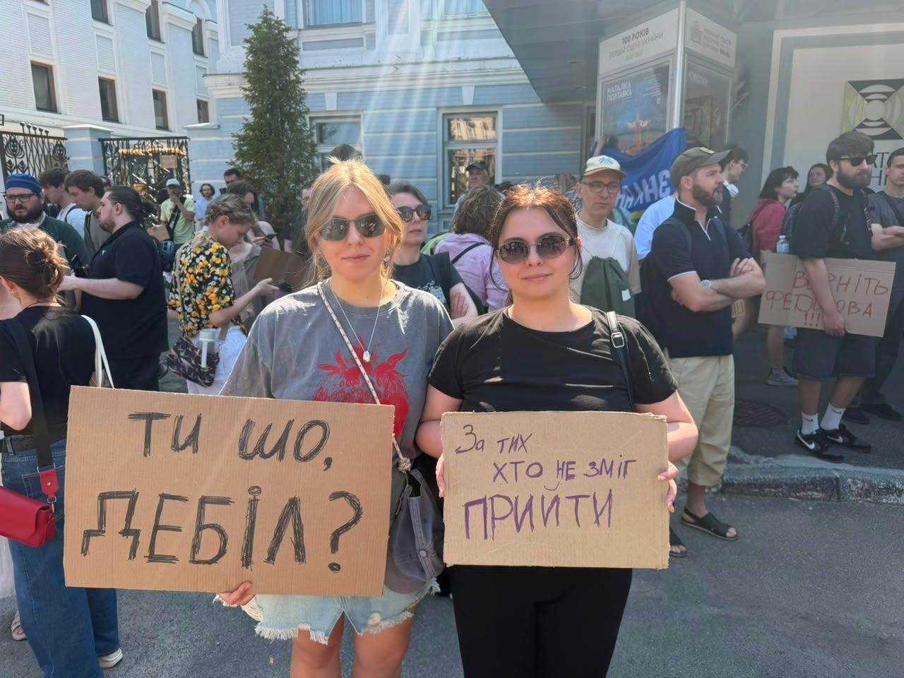 Dos j&oacute;venes manifestantes sostienen carteles que dicen "&iquest;Qu&eacute; est&aacute;s haciendo, idiota?" y "Esto es para todos aquellos que no pudieron estar aqu&iacute;".