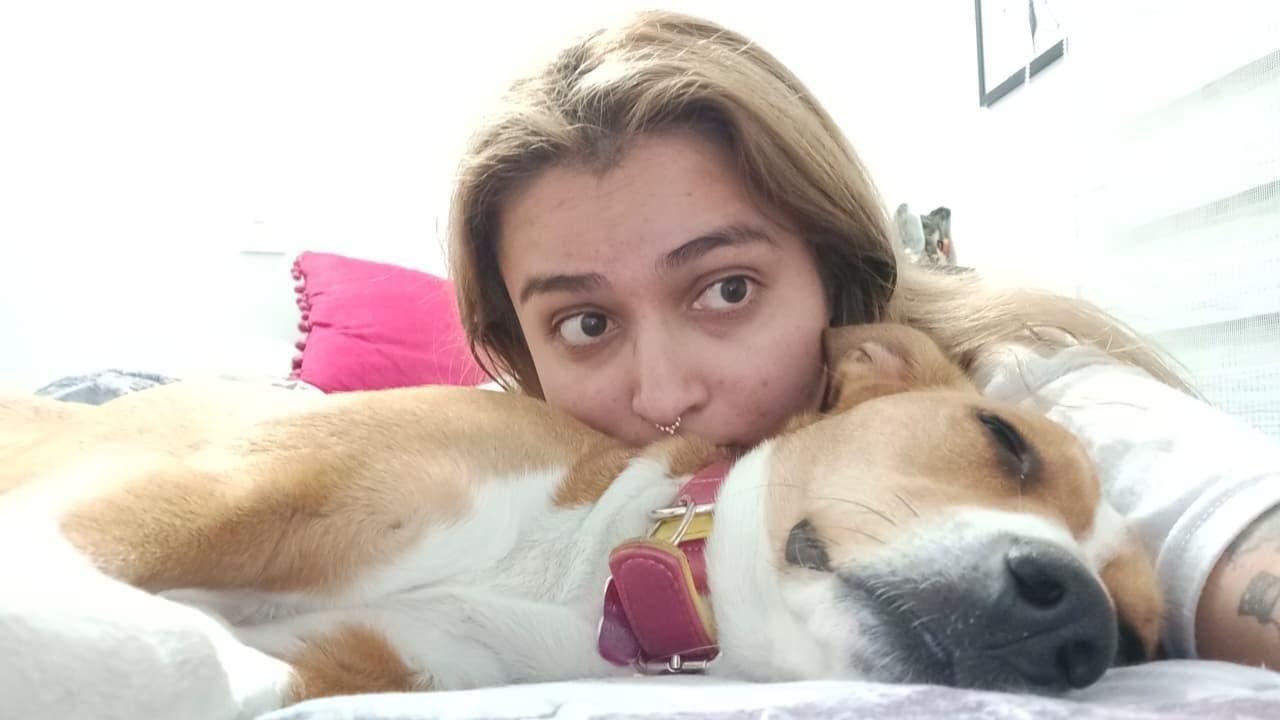 Catalina recuesta su cabeza sobre un perro que est&aacute; dormido sobre una cama y mira a la c&aacute;mara