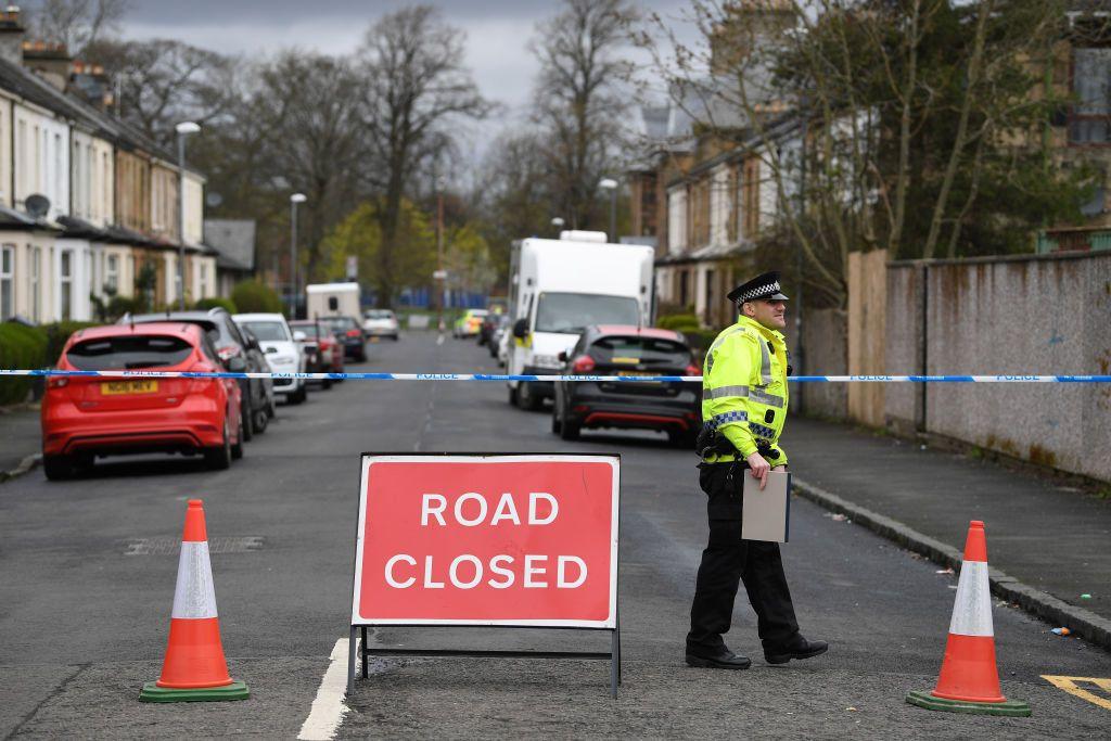Una calle en Glasgow, Escocia, acordonada con cinta azul y blanca de la polic&iacute;a. Un oficial con la distintiva chaqueta fluorescente habla con alguien que est&aacute; fuera del encuadre. 