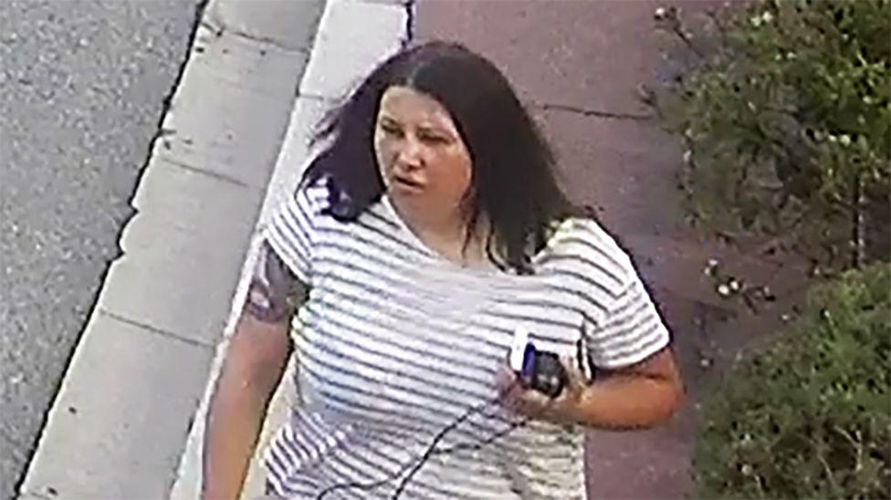 Una mujer de cabello oscuro y expresi&oacute;n seria. Viste una camisa a rayas blancas y negras. En su brazo derecho parece haber un tatuaje de una serpiente y lleva varios objetos en la mano izquierda.
