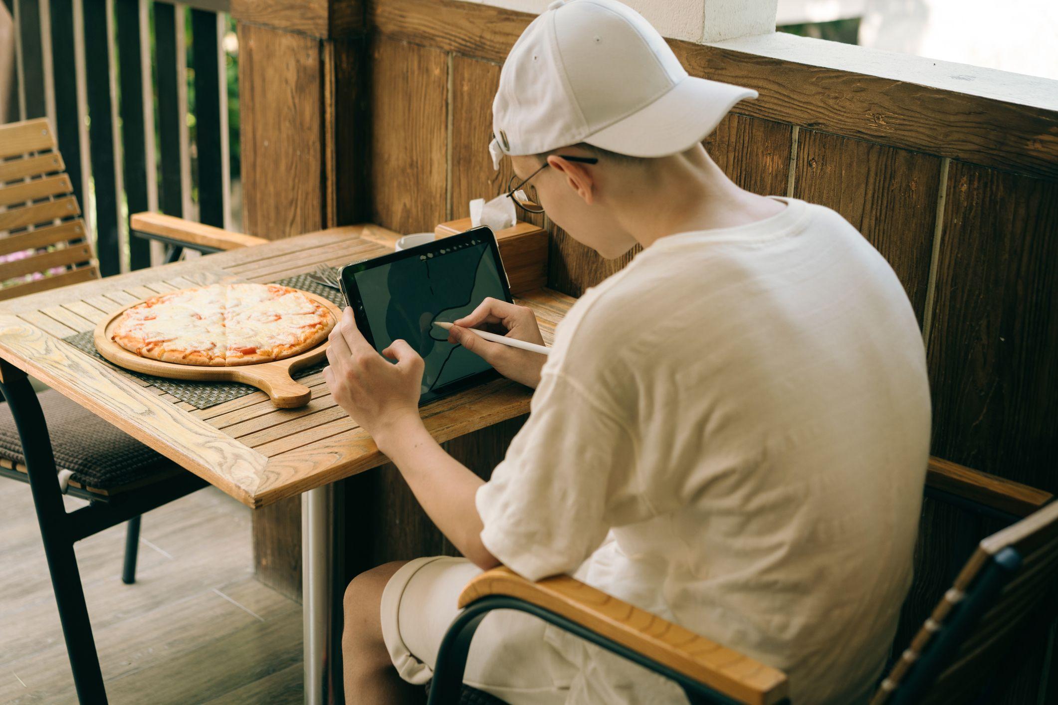 Un joven est&aacute; sentado en una mesa con una tableta con la columna doblada.