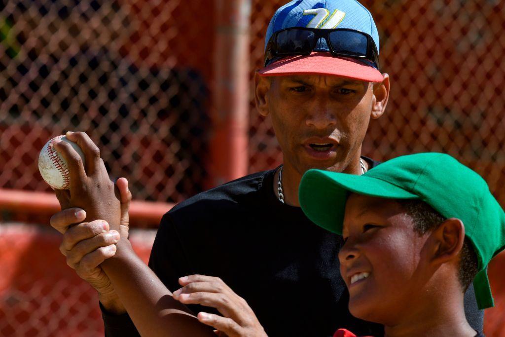 Un entrenador le ense&ntilde;a a un ni&ntilde;o como lanzar la pelota.