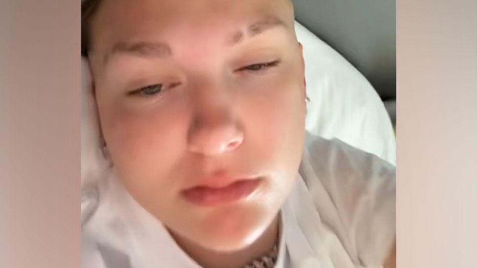 Una selfie de una joven acostada en una cama de hospital.