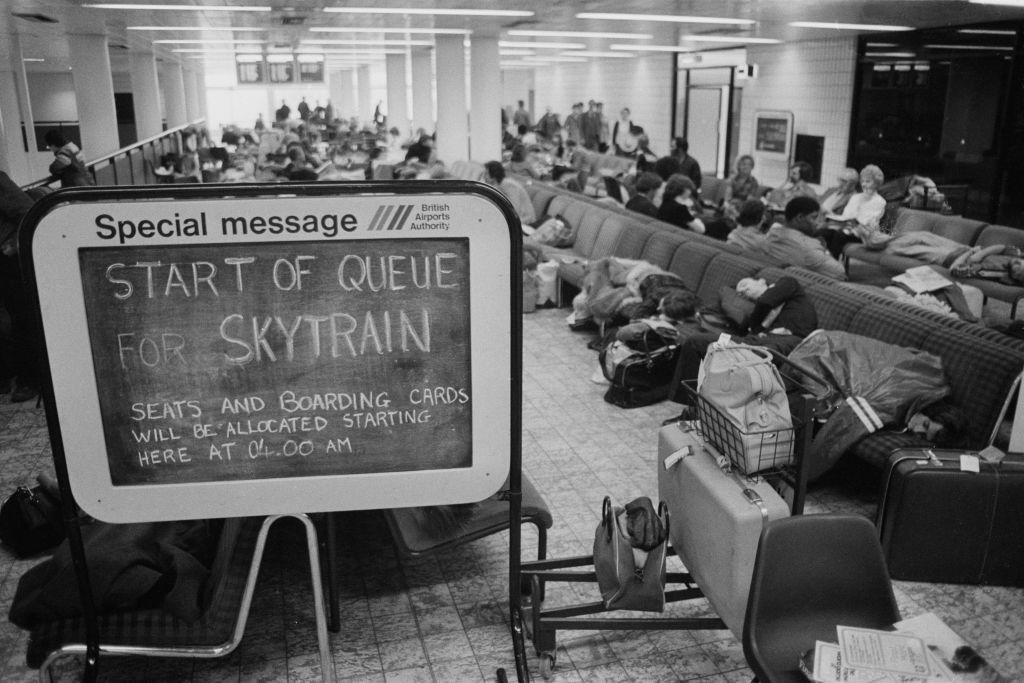 Gente durmiendo en las sillas de un aeropuerto, haciendo fila para poder montarse en un Skytrain.