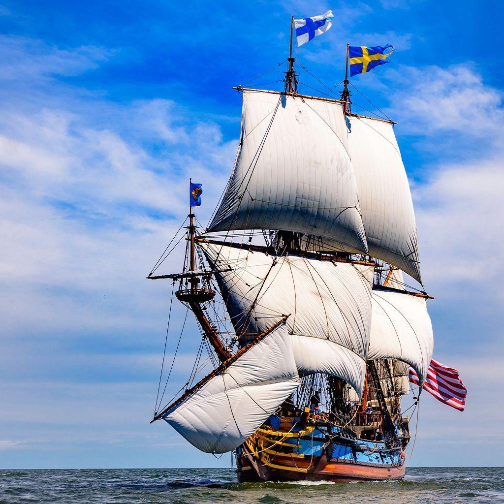 R&eacute;plica de un barco a vela hist&oacute;rico, el Kalmar Nyckel, con velas desplegadas en mar abierto y banderas de Suecia ondeando en lo alto de sus m&aacute;stiles.
