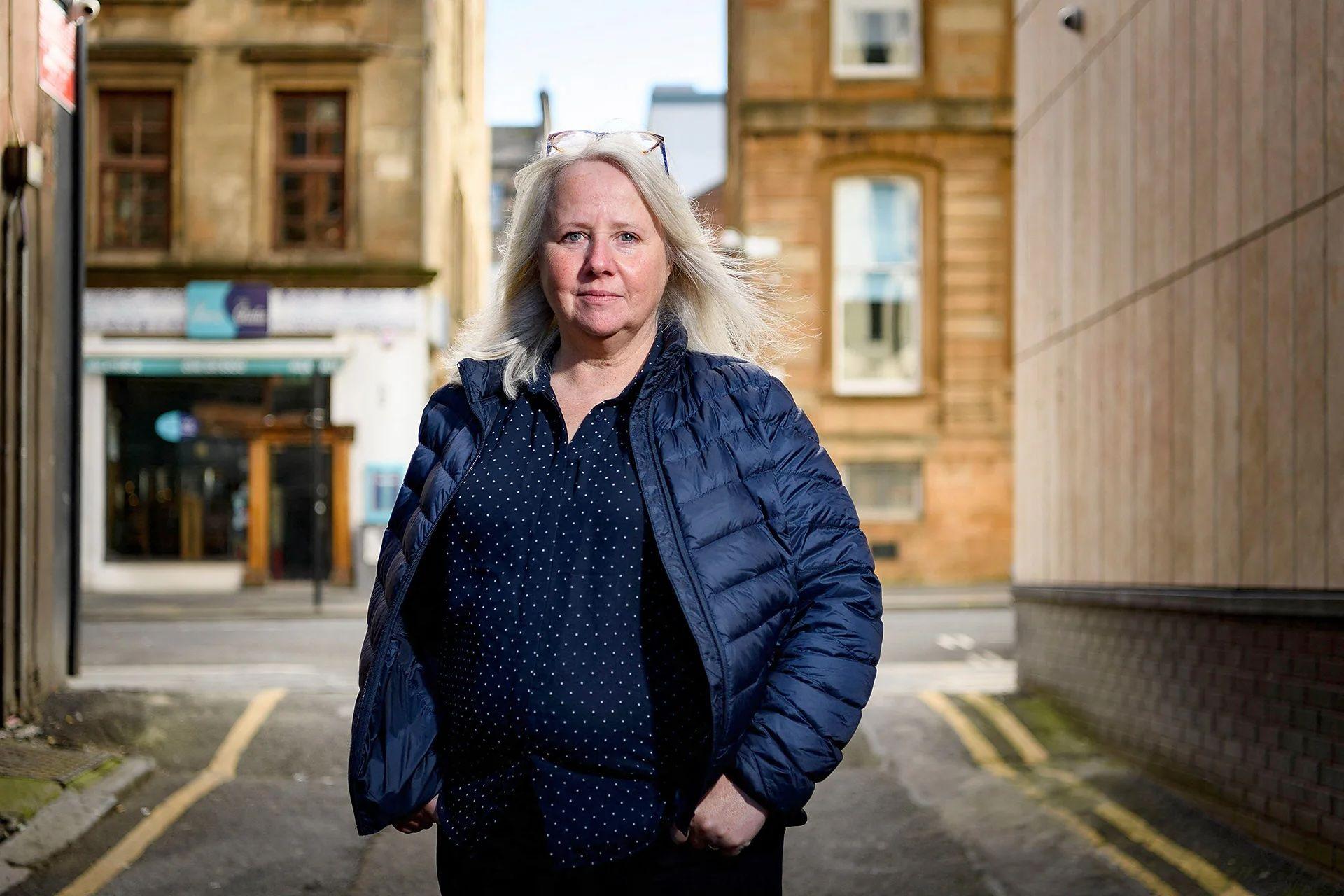 Christine Goodall, cirujana oral, lleva una chaqueta azul y una camisa azul de pepas blancas. Tiene las manos en los bolsillos y mira directo a la c&aacute;mara. 