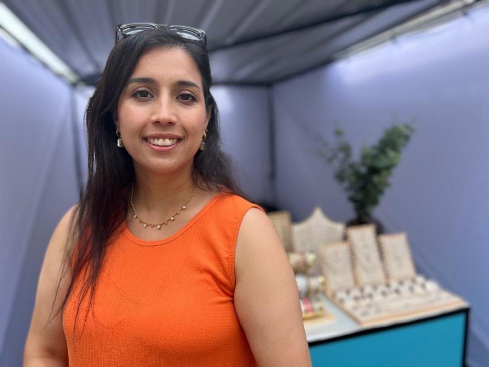 Mujer vestida de naranja frente a su negocio de joyas. 
