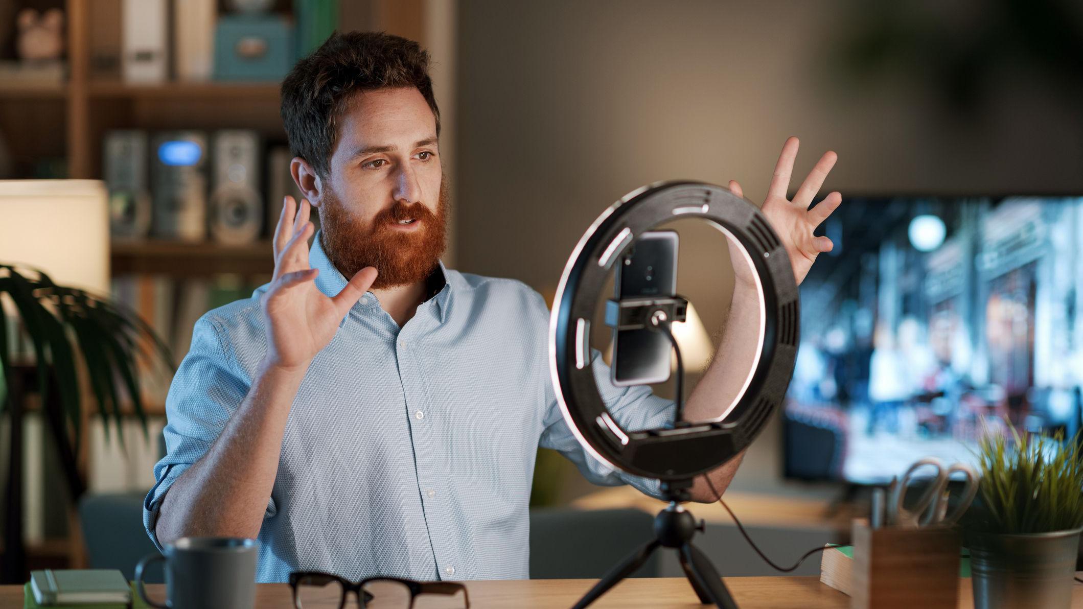 Hombre grabando un video con un tel&eacute;fono y una luz circular detr&aacute;s