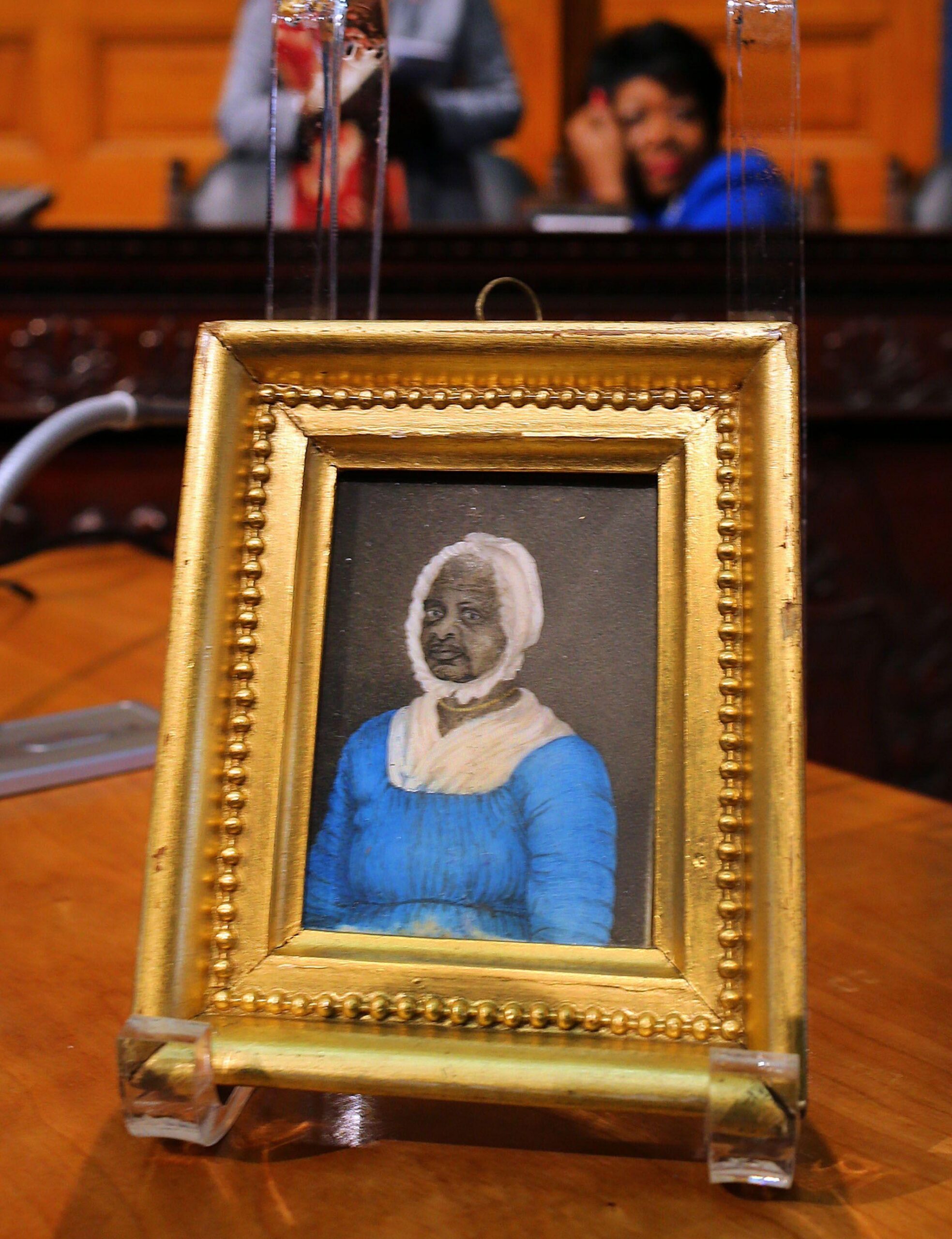 Peque&ntilde;o retrato enmarcado de una persona con vestido azul y cofia blanca, exhibido sobre una mesa.