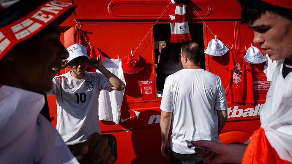 Los aficionados ingleses recogen productos oficiales antes de la tan esperada semifinal del Mundial. 