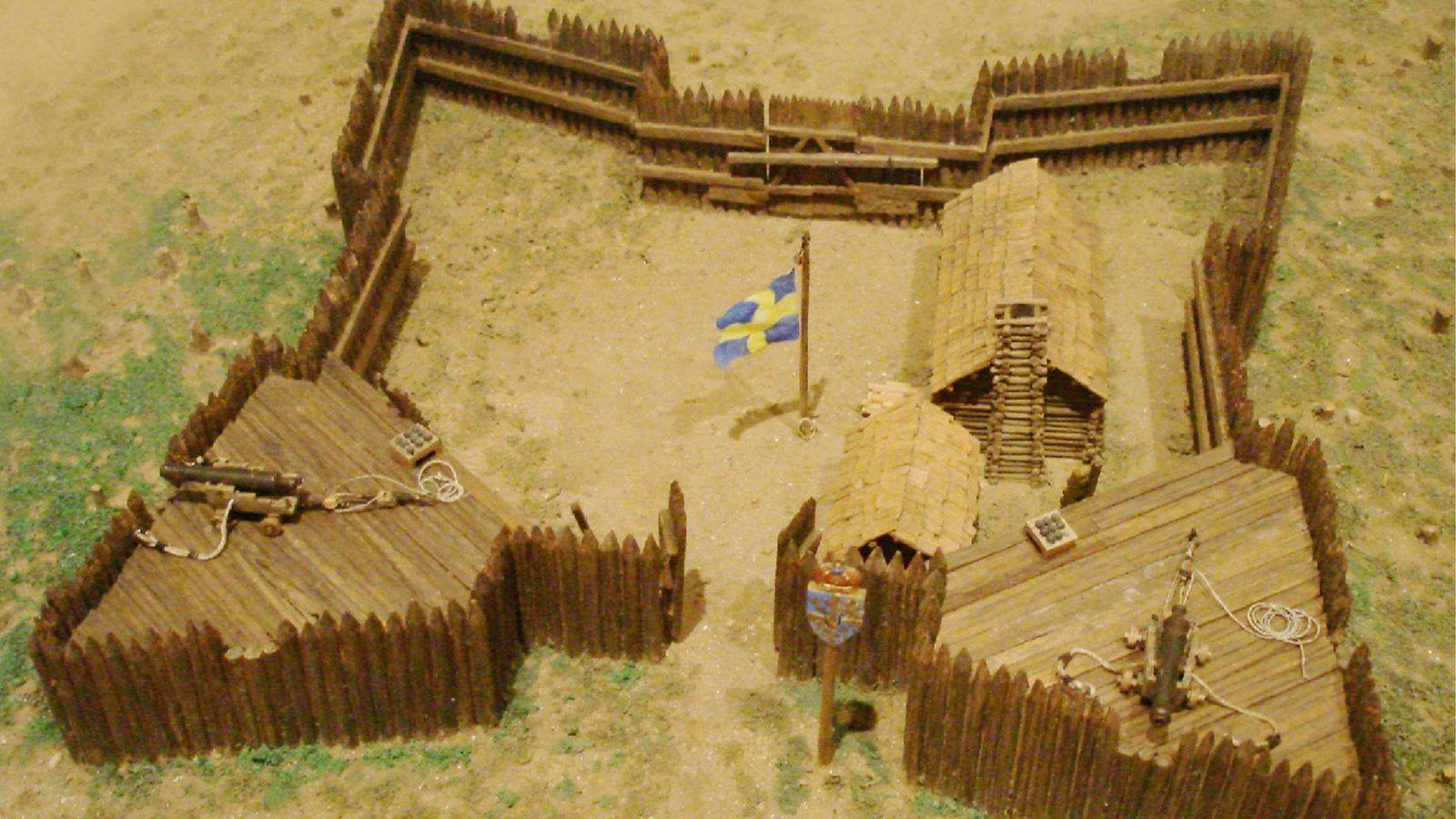 Maqueta de Fuerte Cristina, el primer asentamiento permanente europeo en el valle del Delaware, con empalizadas de madera, edificios de troncos y la bandera sueca en el centro del recinto.
