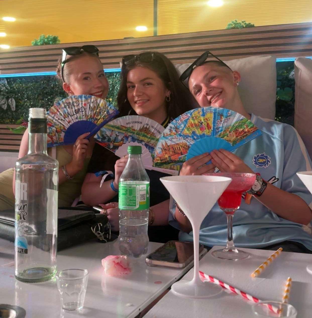 Tres mujeres j&oacute;venes sentadas en un bar, sosteniendo abanicos de papel.