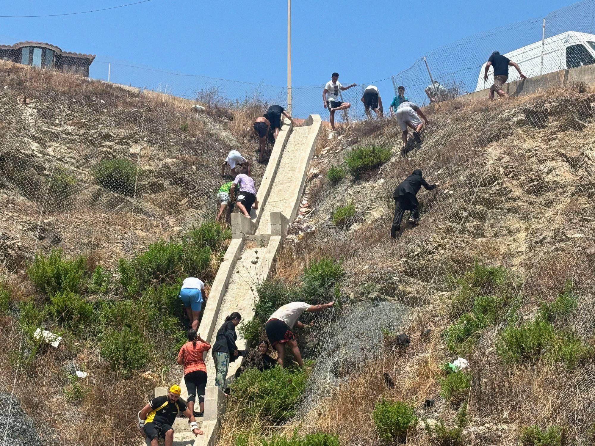 Migrantes trepan por una elevación natural vallada que separa Marruecos de Ceuta.