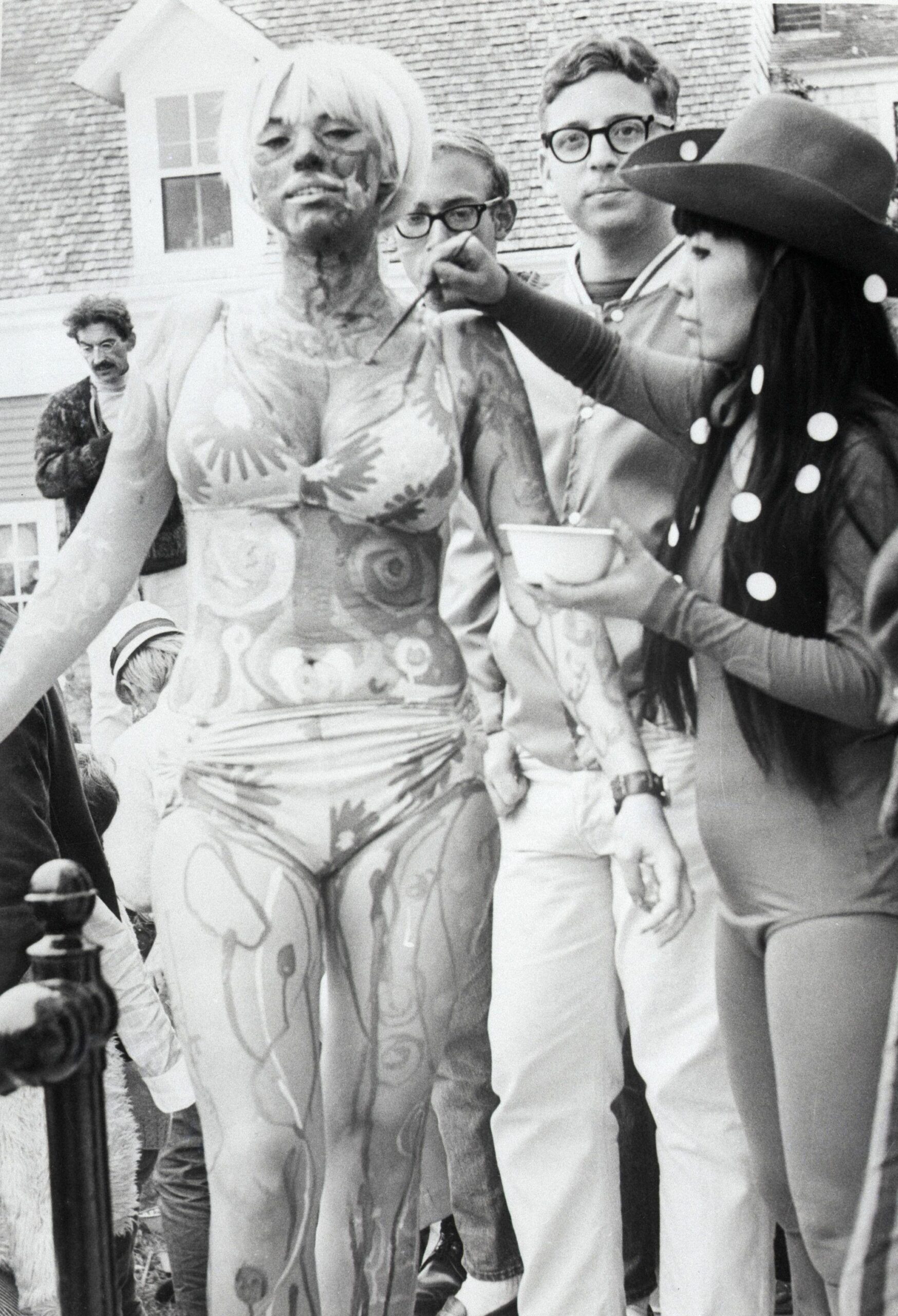 Fotografía en blanco y negro de Yayoi Kusama en 1967 pintando a una joven en bikini en un festival de arte corporal en Provincetown, Massachusetts.
